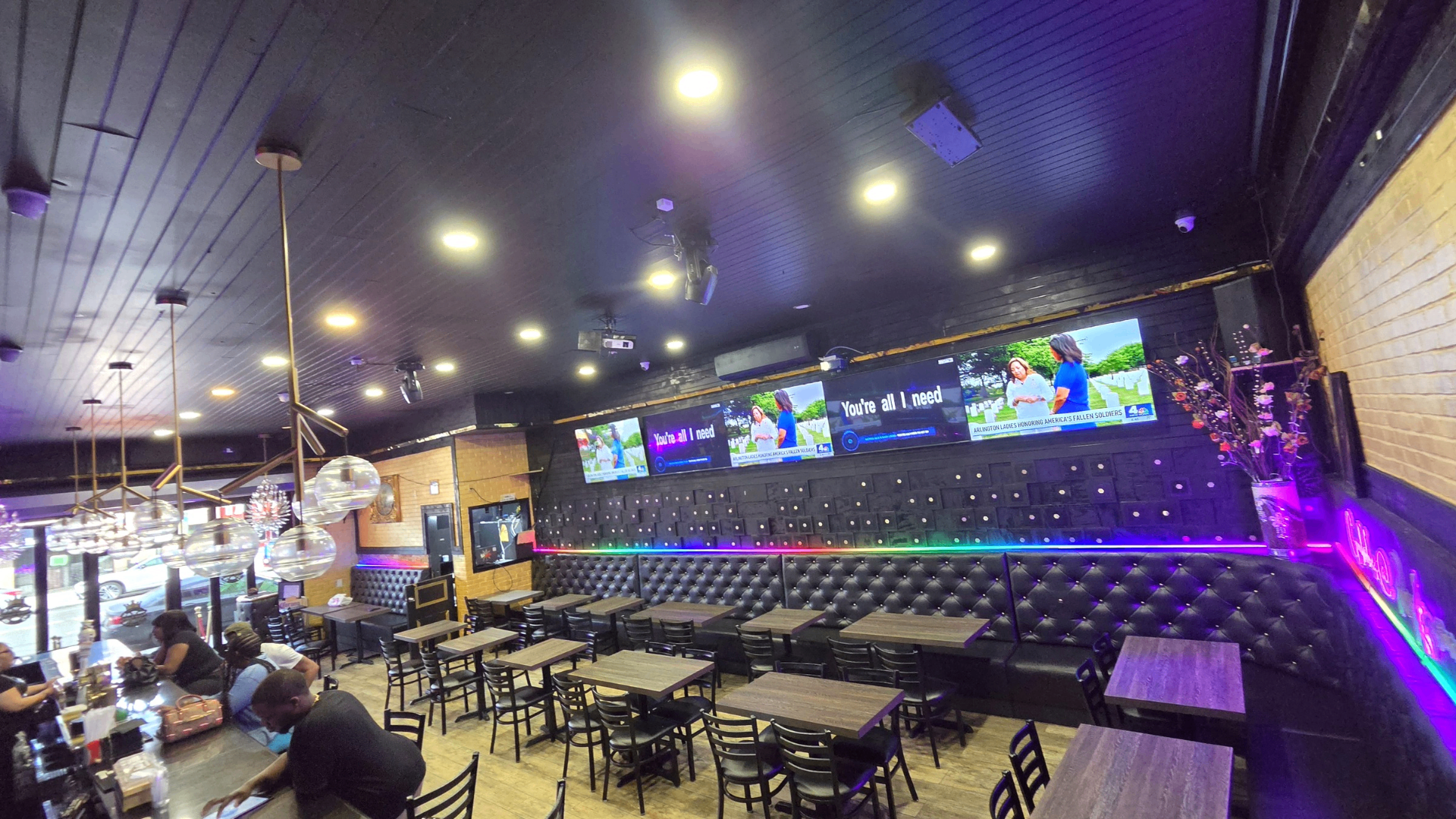 Restaurant dining room with a multi-display TV wall and RGB accent lighting along a tufted booth
