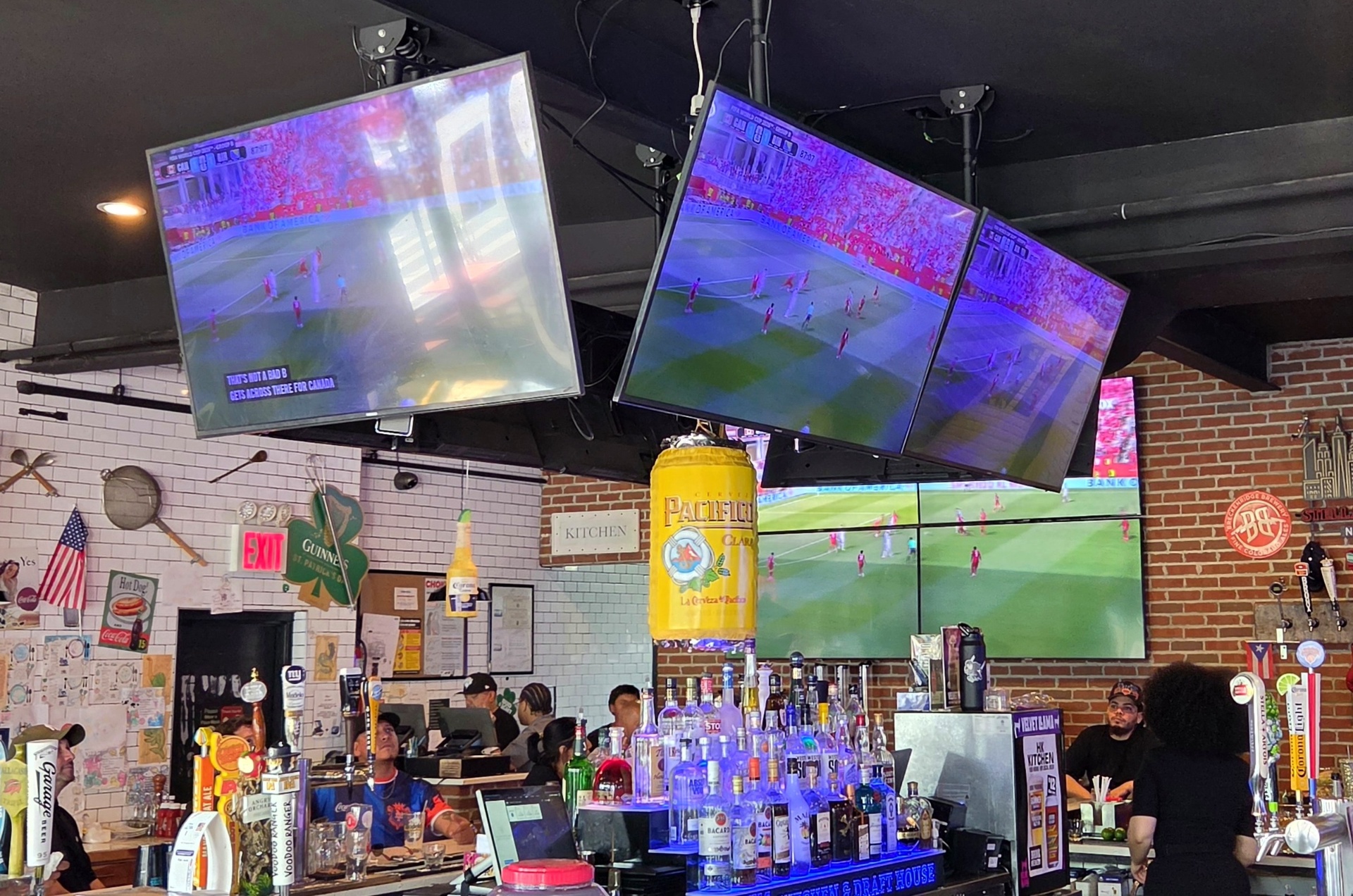 Angled three-screen display cluster showing a live game at a sports bar