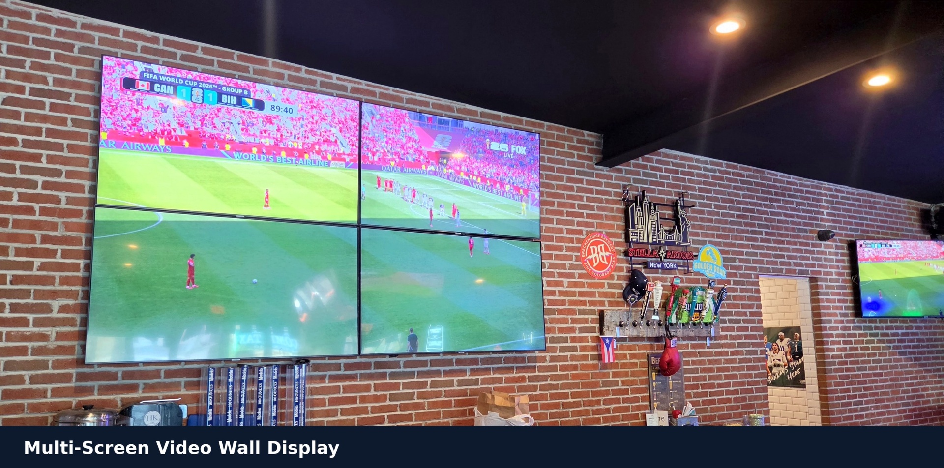 Four-screen video wall mounted on exposed brick at a sports bar, each display showing a live game
