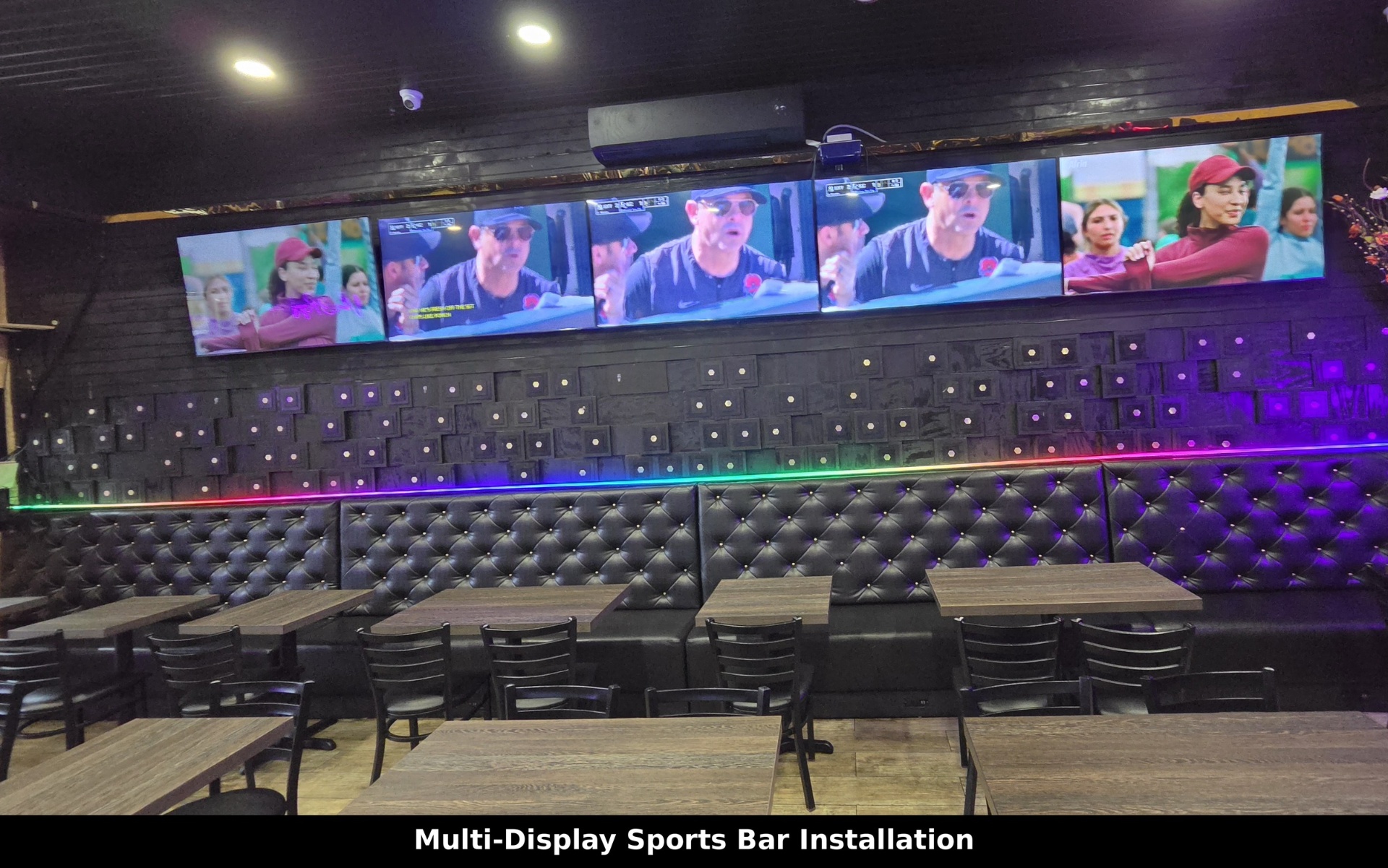 Five-screen TV wall above a tufted leather booth with RGB accent lighting at a sports bar